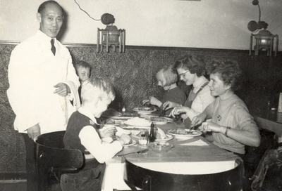 878017 Portret van Jih Peng Chen (1902), bij een tafeltje met jongeren in zijn Chinees restaurant Shanghai ...